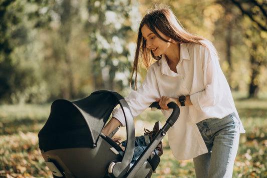 A young mother smiling while pushing her baby in a modern black baby stroller.