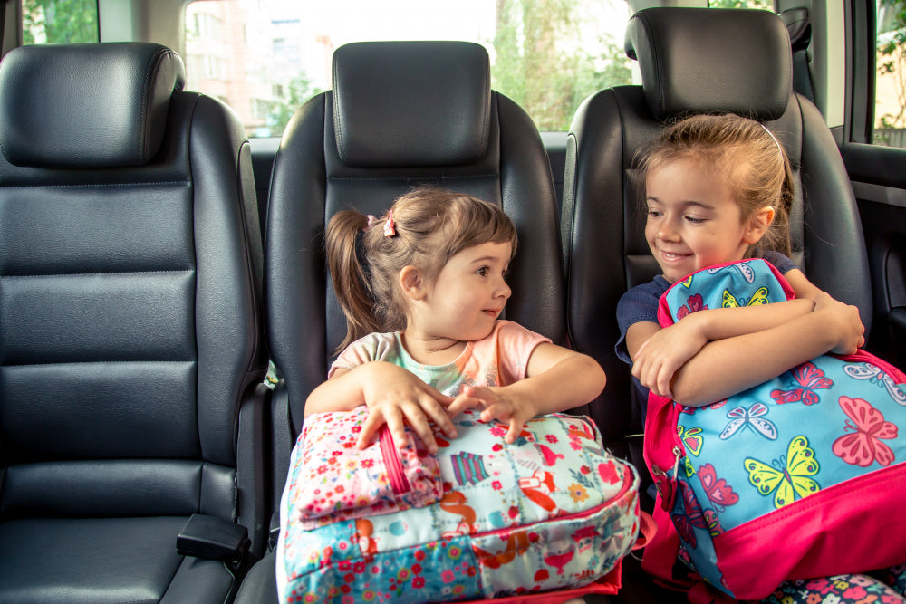 Two children sitting in a car holding colorful backpacks.